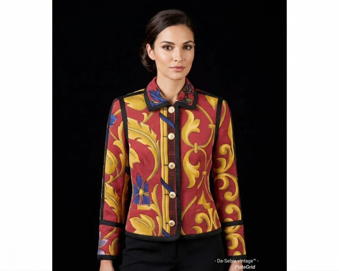 A woman modeling a Gianni Versace Baroque cropped jacket with a bold baroque-style pattern in red, yellow, and blue, featuring gold buttons and black trim, set against a solid black background.