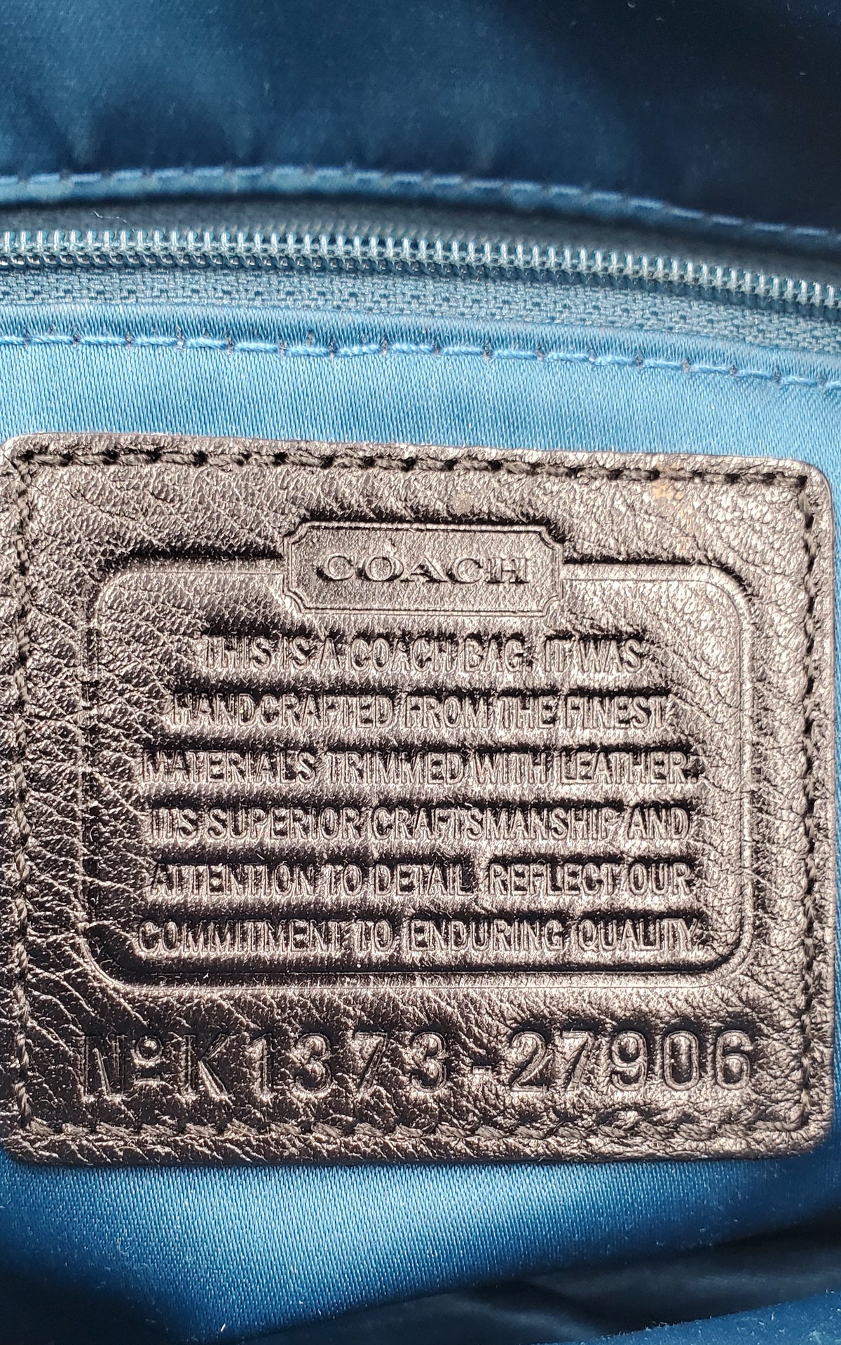 Close-up of a Coach interior label patch on a blue nylon bag, showing embossed text and a stitched leather-like brand tab.