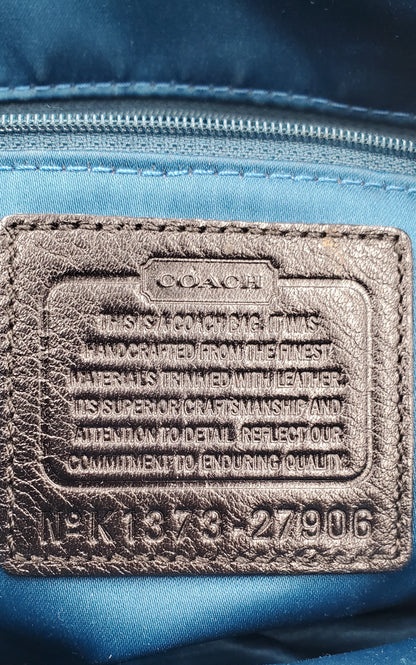 Close-up of a Coach interior label patch on a blue nylon bag, showing embossed text and a stitched leather-like brand tab.