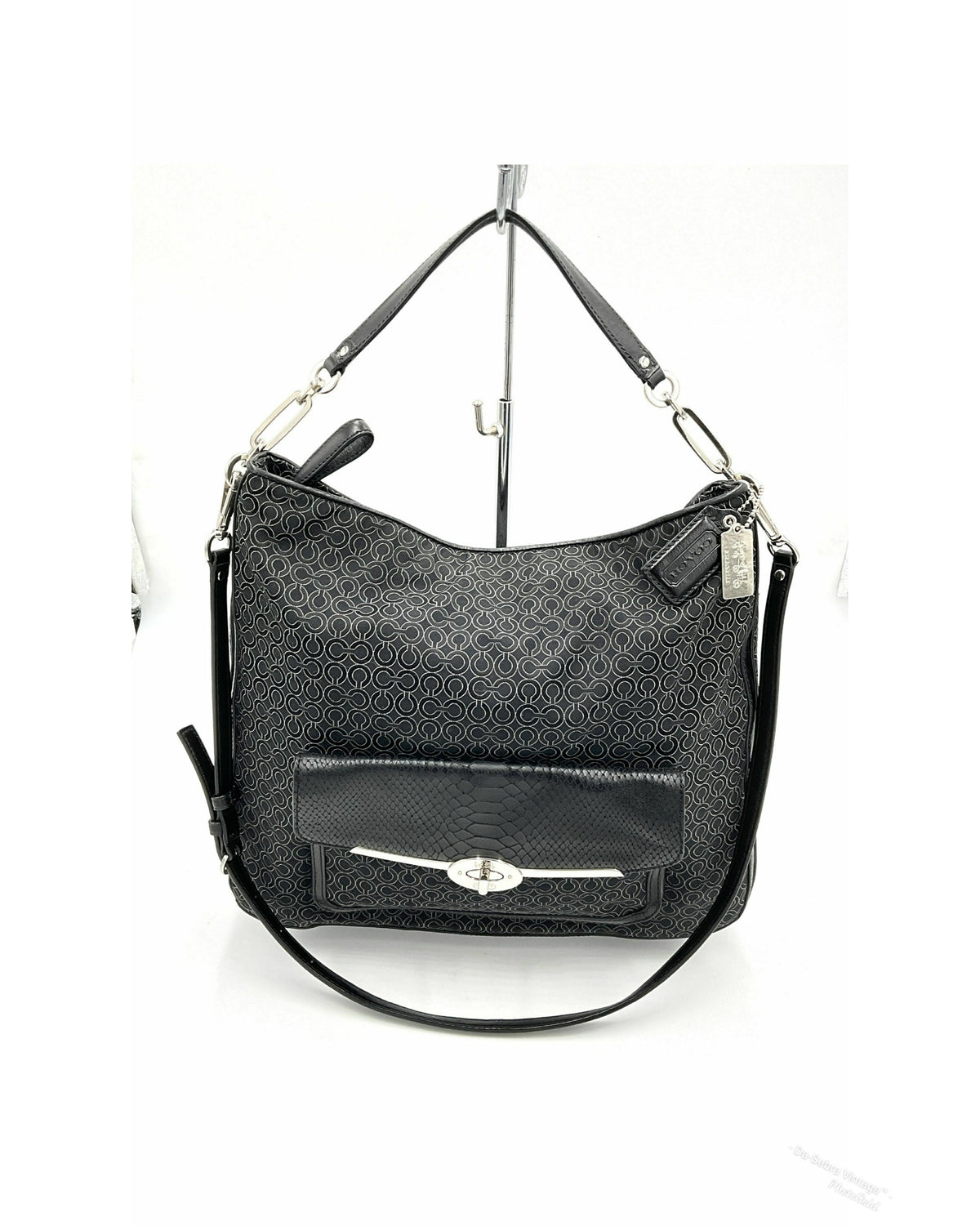 A black jacquard Coach hobo shoulder bag with a textured monogram pattern, a front flap pocket with a silver-tone turn-lock closure, and a detachable shoulder strap, displayed on a white background stand.