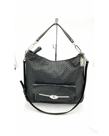 A black jacquard Coach hobo shoulder bag with a textured monogram pattern, a front flap pocket with a silver-tone turn-lock closure, and a detachable shoulder strap, displayed on a white background stand.