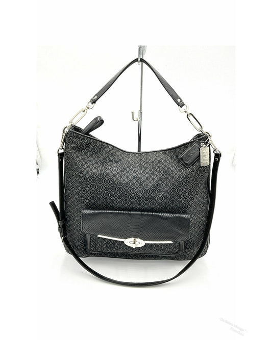 A black jacquard Coach hobo shoulder bag with a textured monogram pattern, a front flap pocket with a silver-tone turn-lock closure, and a detachable shoulder strap, displayed on a white background stand.