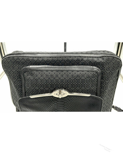 A close-up of a black jacquard Coach handbag featuring a textured geometric pattern on the main body and a front zip pocket with a silver-tone turn-lock clasp, set against a white background.
