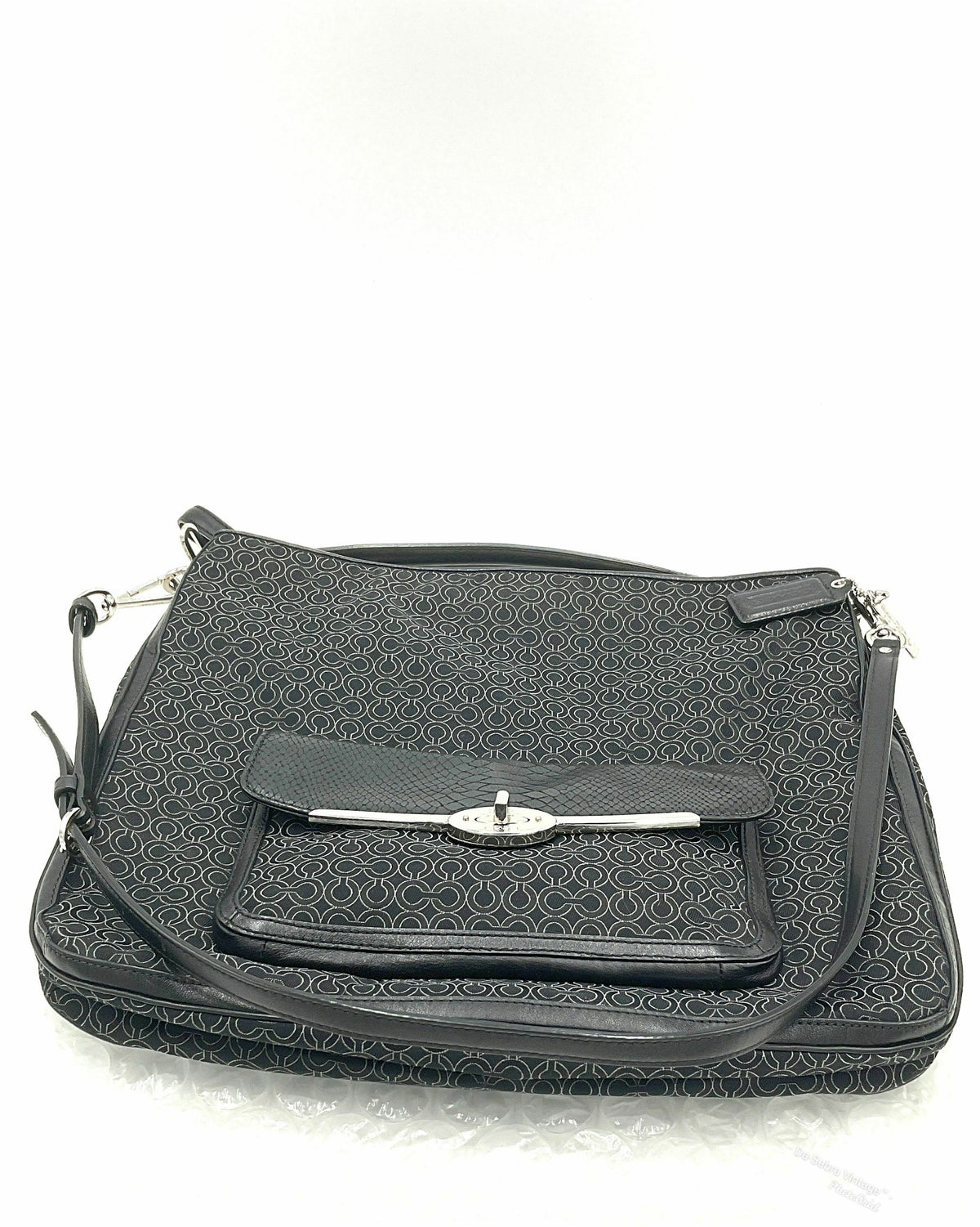 A Coach black jacquard shoulder bag with a textured geometric pattern, featuring a front flap pocket with a silver-tone metal clasp and a top handle, set against a plain white background.