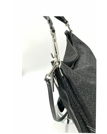 Close-up of a black Coach textured  jacquard shoulder bag with a repeating circular monogram pattern, silver-tone hardware, and a black leather strap on a white background.