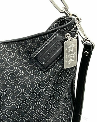 Close-up of a Coach black jacquard handbag with an allover embossed monogram pattern, a black leather brand tab, and a silver metal hangtag on a white background.
