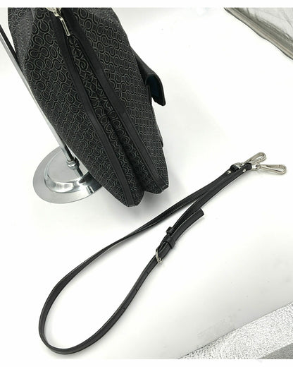 A Coach black jacquard patterned handbag with a detachable black leather wristlet strap and silver-tone hardware, displayed on a white surface next to a silver stand.