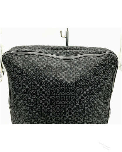 A black jacquard Coach bag with a repeating white monogram pattern, featuring a top zipper and a metal hanger hook inserted at the top, set against a plain white background.