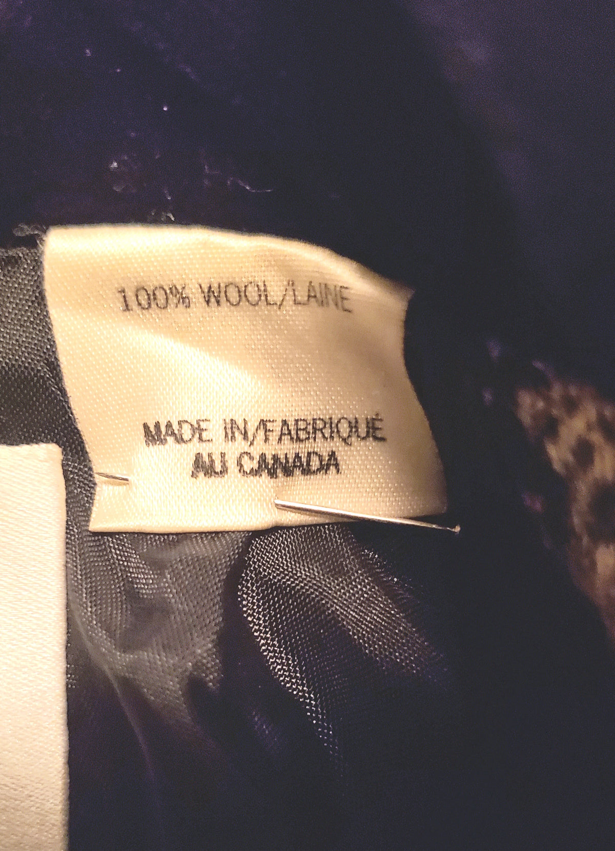 Close-up of a sewn-in fabric label reading '100% WOOL/LAIN' and 'MADE IN/FABRIQUÉ AU CANADA' attached to dark  black fabric lining.