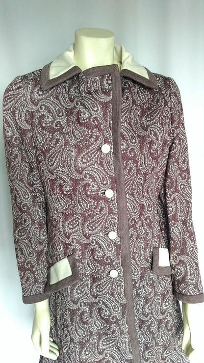 A vintage patterned coat displayed on a mannequin.  The coat features a brown and beige paisley pattern with solid brown trim and a cream-colored collar and pocket flaps.