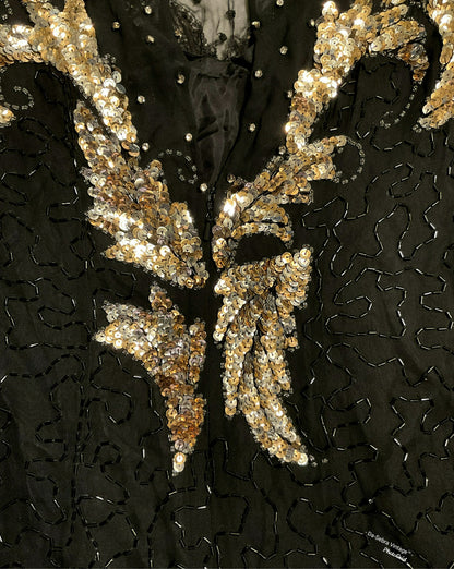 Close-up of a black embellished garment featuring large metallic gold sequined wing  with silver rhinestone accents and black embroidered detailing.
