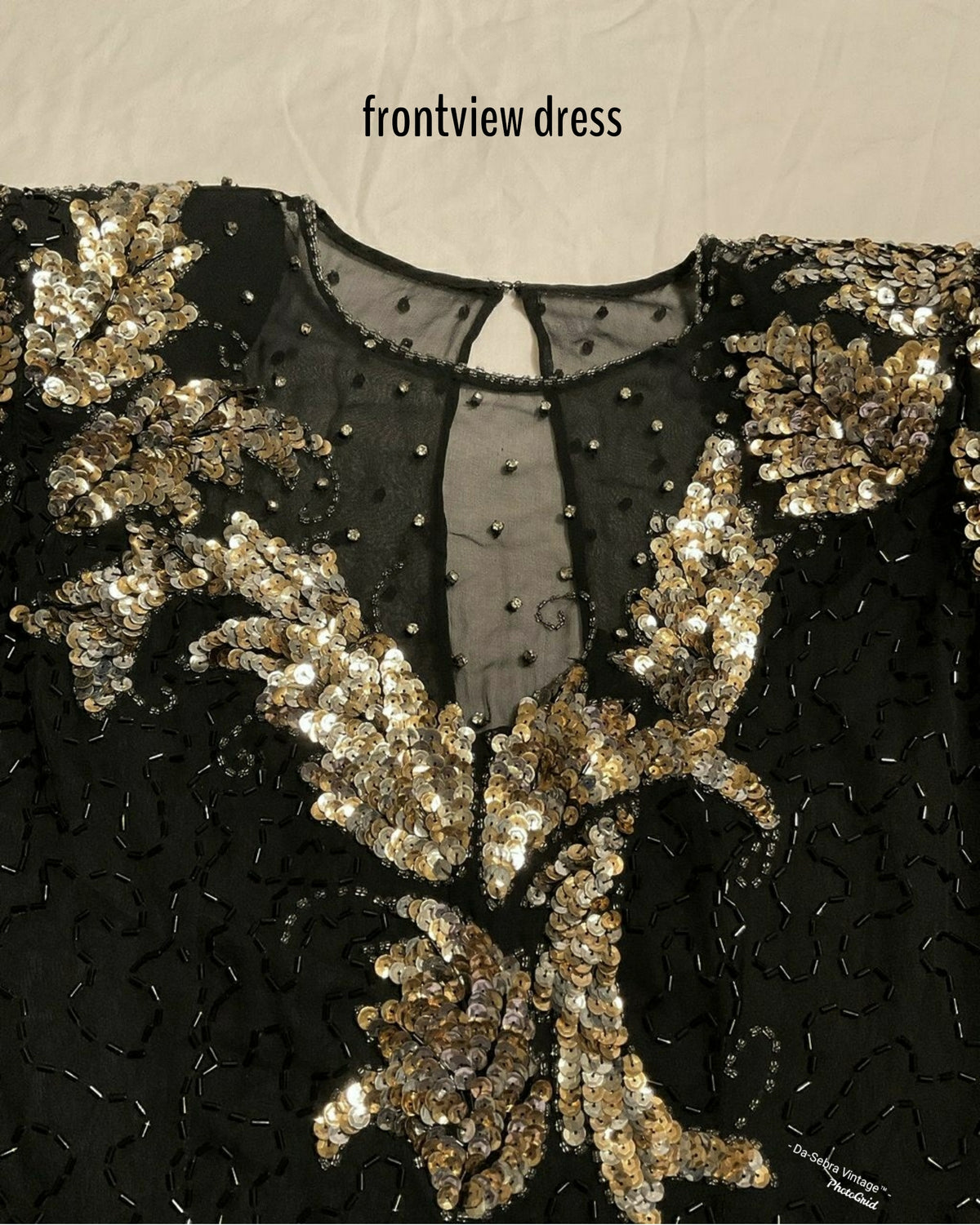 Close-up of a black embellished dress with ornate gold sequin and bead floral detailing, shown from the front with a sheer neckline and small text reading 'frontview dress' at the top.