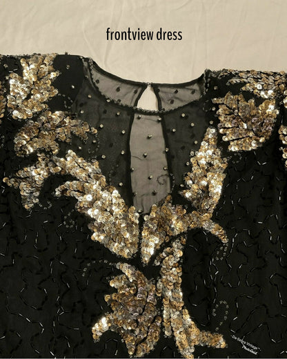 Close-up of a black embellished dress with ornate gold sequin and bead floral detailing, shown from the front with a sheer neckline and small text reading 'frontview dress' at the top.