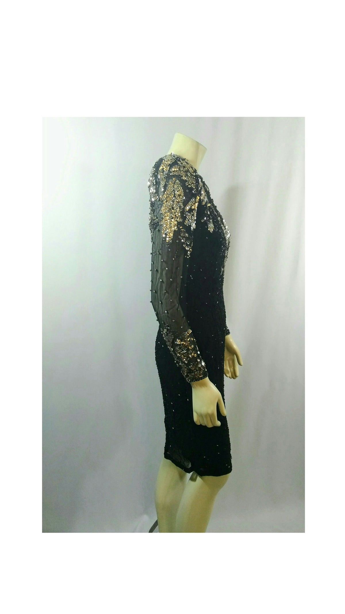 A black long-sleeve dress with gold sequined detailing on the bodice and sleeves, displayed on a mannequin against a light gray backdrop.