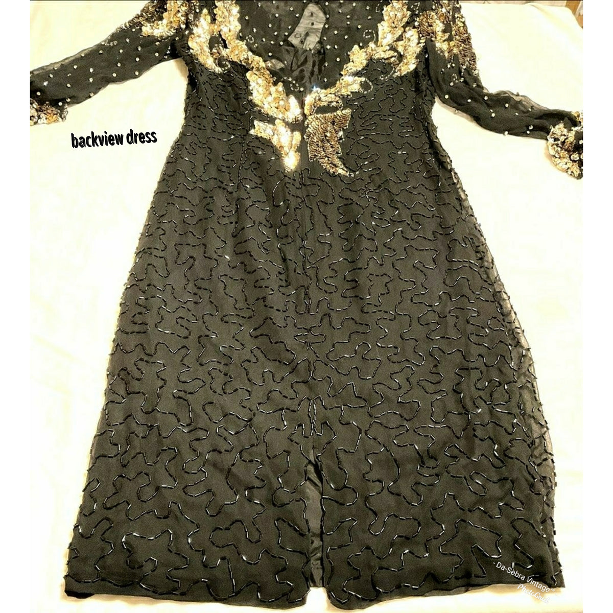 Close up to view beading on Black long-sleeve dress with gold sequin embroidery and beaded detailing, shown from the back on a light fabric background.