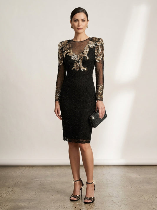 A woman models a black  knee-length dress with sheer long embellished sleeves and ornate gold floral embroidery across the bodice and sleeves. She is standing against a neutral studio wall, holding a small black clutch and wearing black strappy heels.