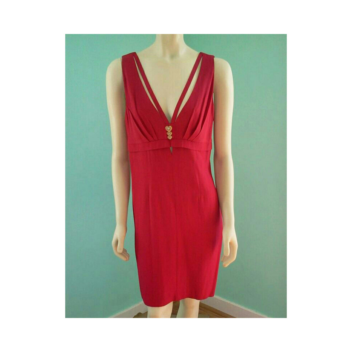 A red sleeveless knee-length dress with a deep V-neckline and crossover straps, displayed on a mannequin against a teal wall.