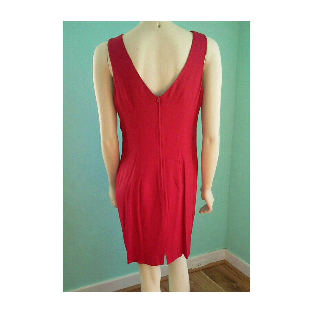 A sleeveless red dress with a deep V-neckline and a front zipper, displayed on a mannequin against a light teal wall.