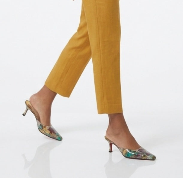 A person wearing cropped mustard-yellow trousers and square toe mule heels, shown against a clean white studio background.