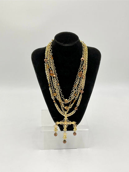 A multi-strand gold chain necklace with brown beads and a gold cross pendant, displayed on a black velvet jewelry bust stand.