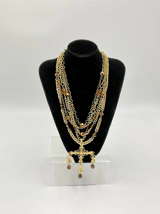 A multi-strand gold chain necklace with brown beads and a gold cross pendant, displayed on a black velvet jewelry bust stand.