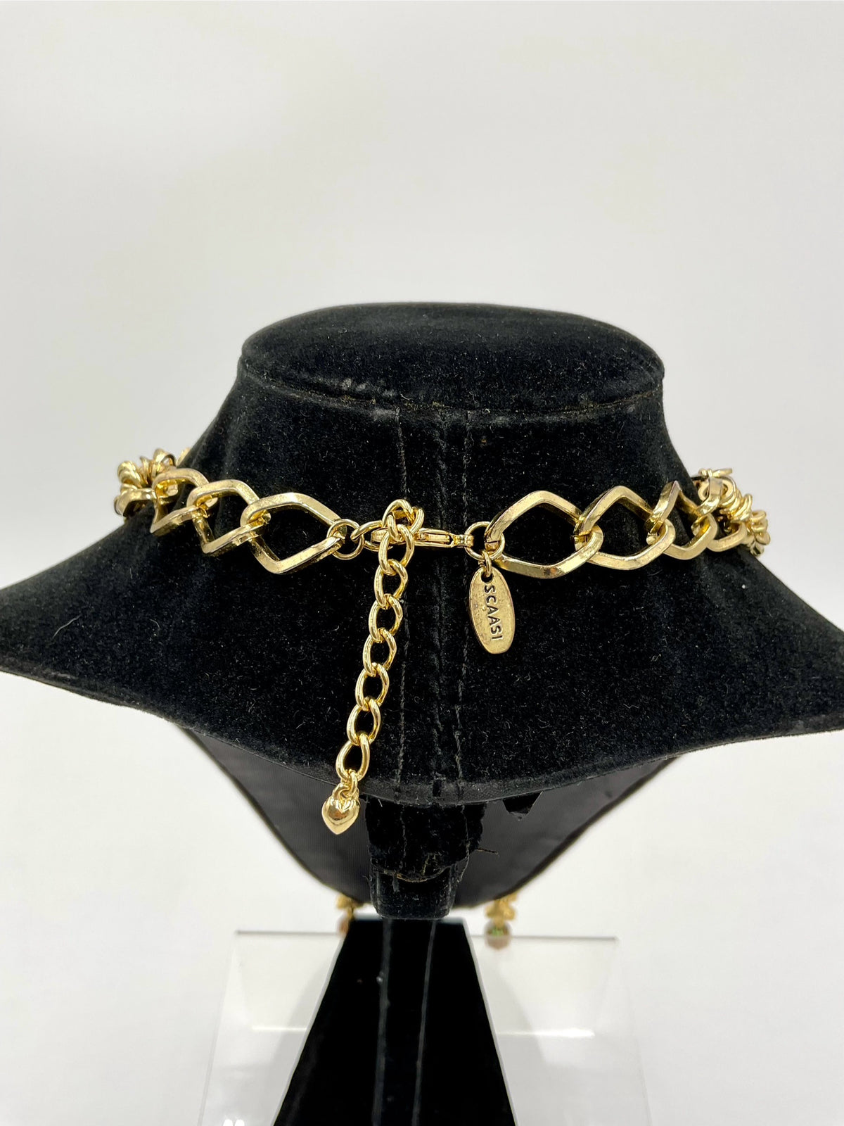 A gold-tone chain choker necklace with a signature interlocking link design and a dangling clover charm, displayed on a black velvet jewelry bust.