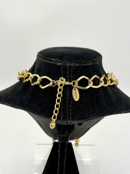 A gold-tone chain choker necklace with a signature interlocking link design and a dangling clover charm, displayed on a black velvet jewelry bust.