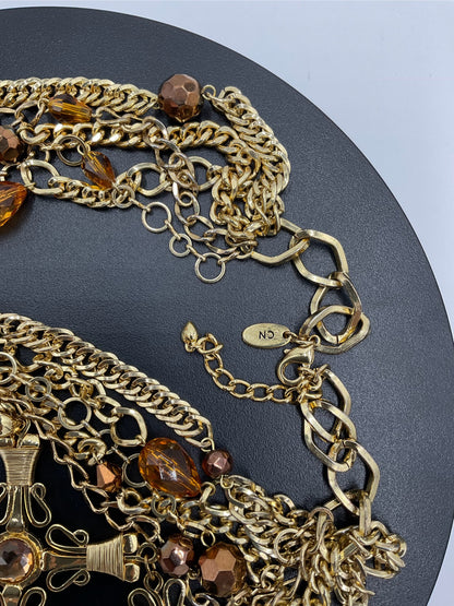 A close-up of a chunky gold-tone chain necklace with faceted amber-brown beads and links, displayed on a dark round surface.