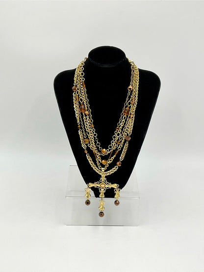 A multi-layered gold chain necklace with brown beads and a cross pendant, displayed on a black neck mannequin bust over a clear acrylic stand against a white background.