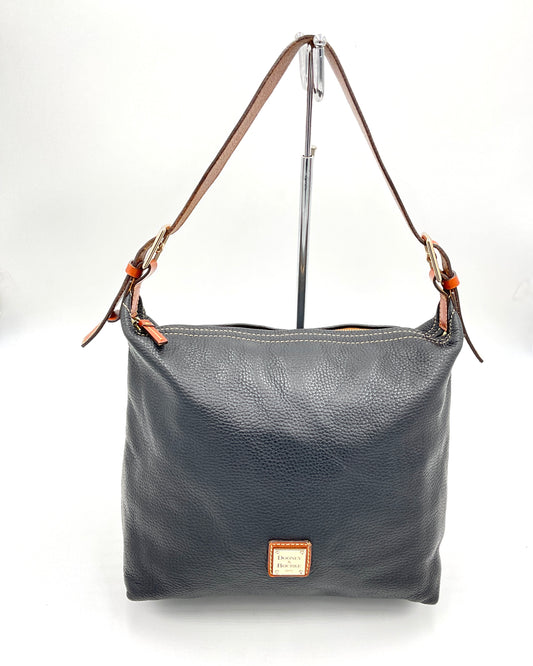 A dark black pebbled leather shoulder bag with brown leather straps and a small tan Dooney & Bourke brand plaque on the front, displayed on a stand against a white background.