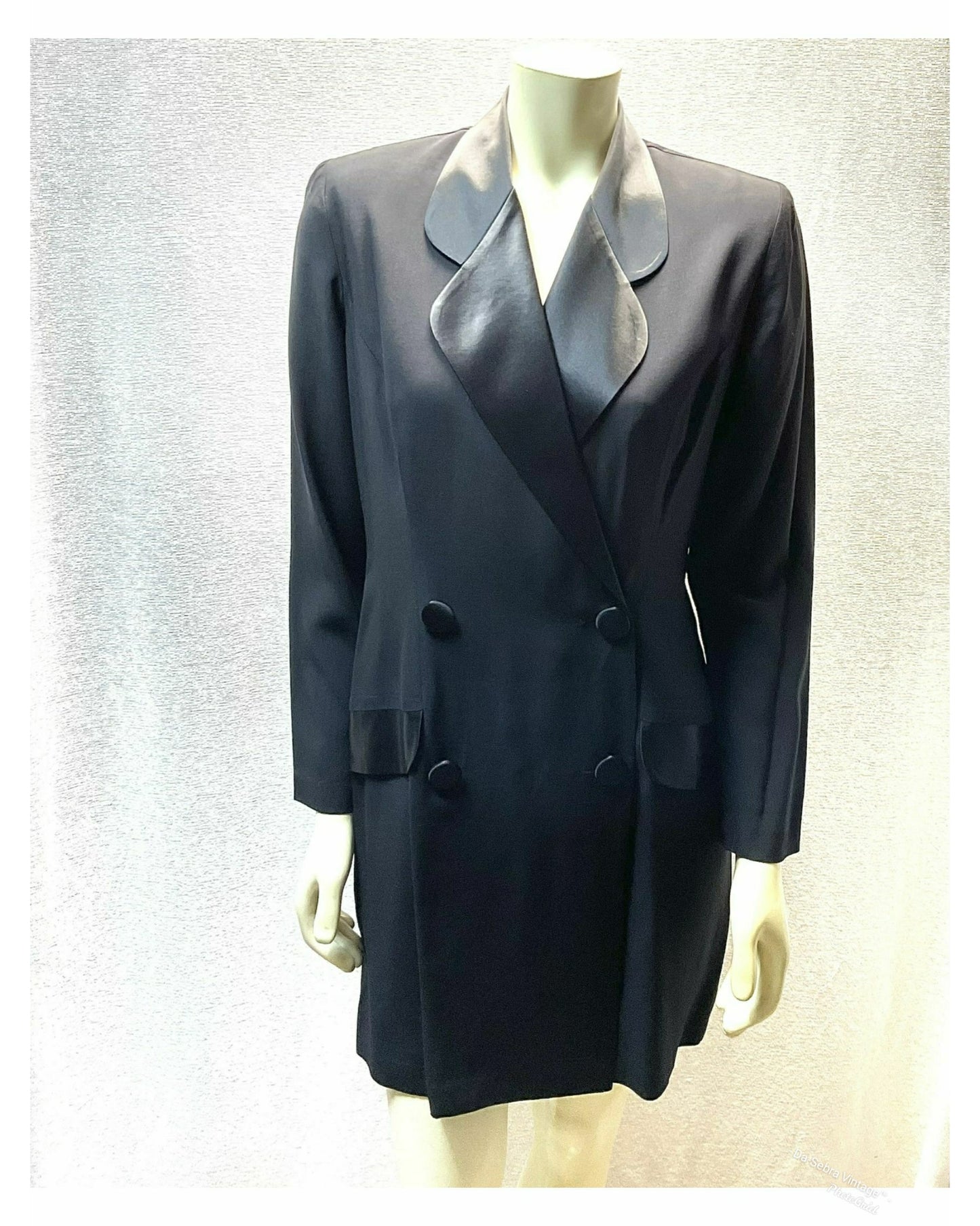 A black double-breasted tuxedo Style front Skort Romper with black satin lapels, displayed on a mannequin against a textured light white background.