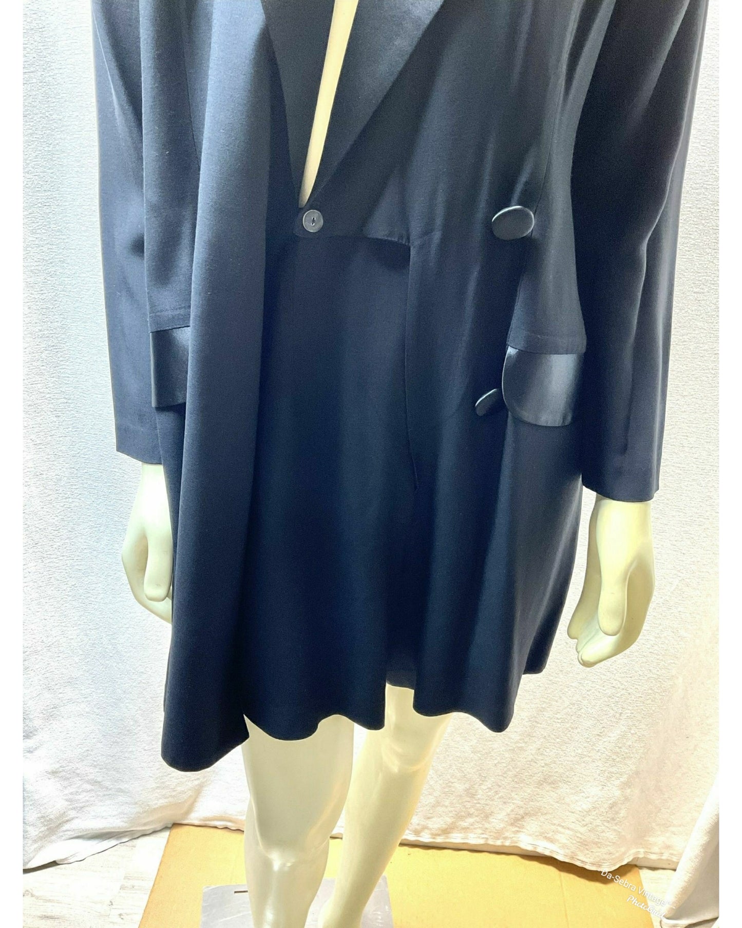 A black double-breasted tuxedo Style front Skort Romper with black satin lapels, displayed on a mannequin against a textured light white background.