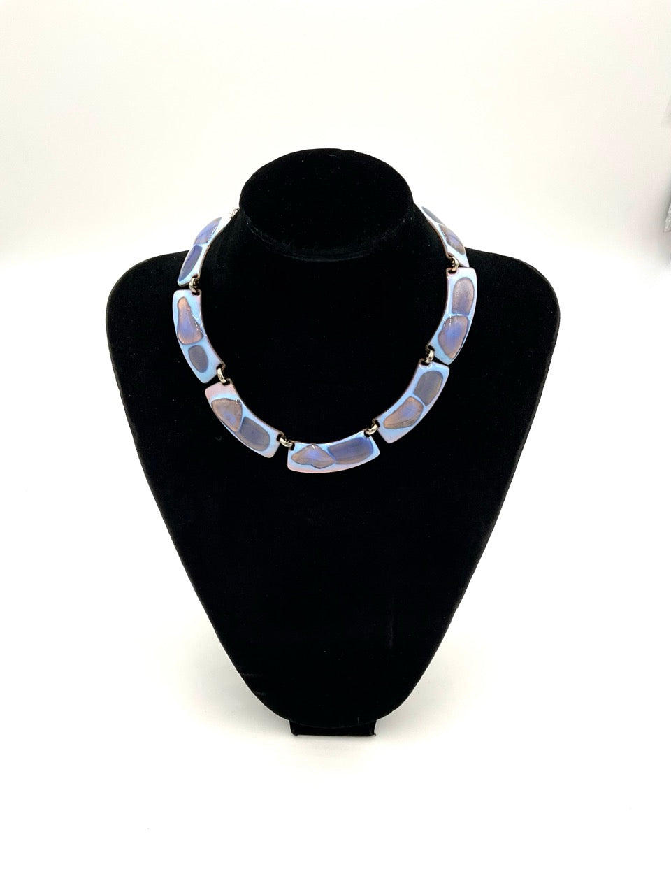 The necklace color palette is exceptional: a striking opalescent blue enamel with beautiful hints of lavender and purple tones. displayed on a black velvet jewelry bust against a white background.