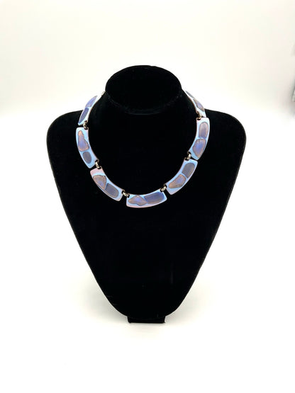 The necklace color palette is exceptional: a striking opalescent blue enamel with beautiful hints of lavender and purple tones. displayed on a black velvet jewelry bust against a white background.