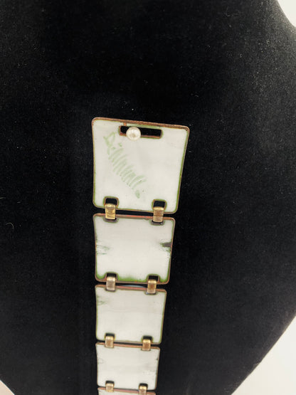 A close-up of a vintage-style bracelet  with signature,  featuring rectangular white enamel links with gold-toned metal borders and connectors, displayed on a black velvet jewelry bust.