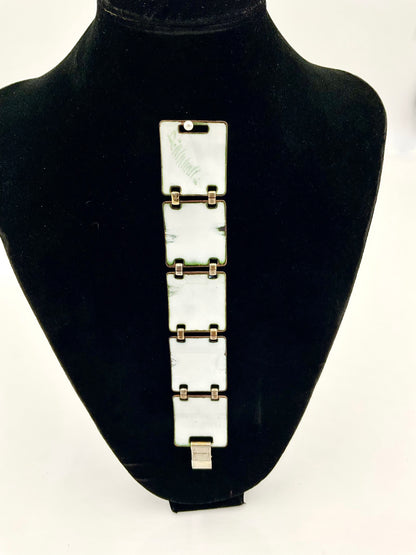 A silver-toned metal link bracelet displayed on a black velvet jewelry bust against a white background.