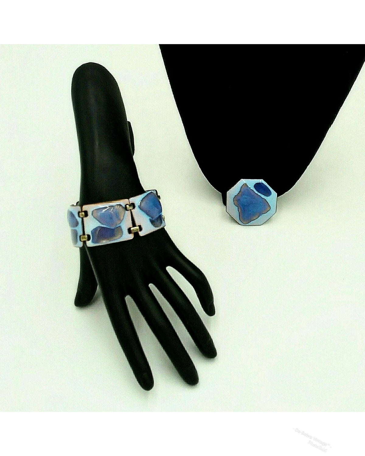 The bracelet and brooch color palette is exceptional: a striking opalescent blue enamel with beautiful hints of blue, lavender and purple tones.  displayed on a black mannequin hand,  black mannequin arm against a white background.