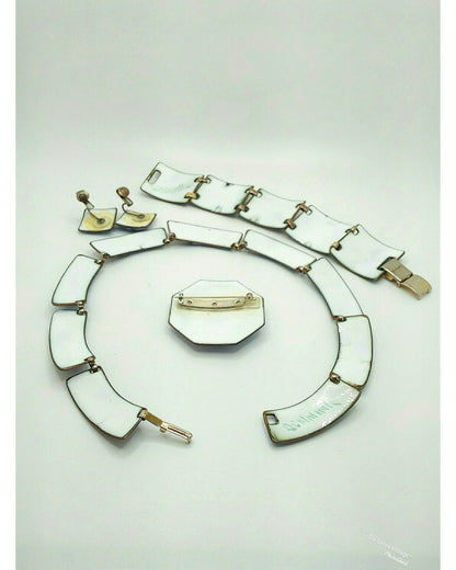 A vintage jewelry set featuring white enamel  geometric links with gold-tone metal settings, including a bracelet, necklace, earrings, and a pin, displayed on a light gray background.