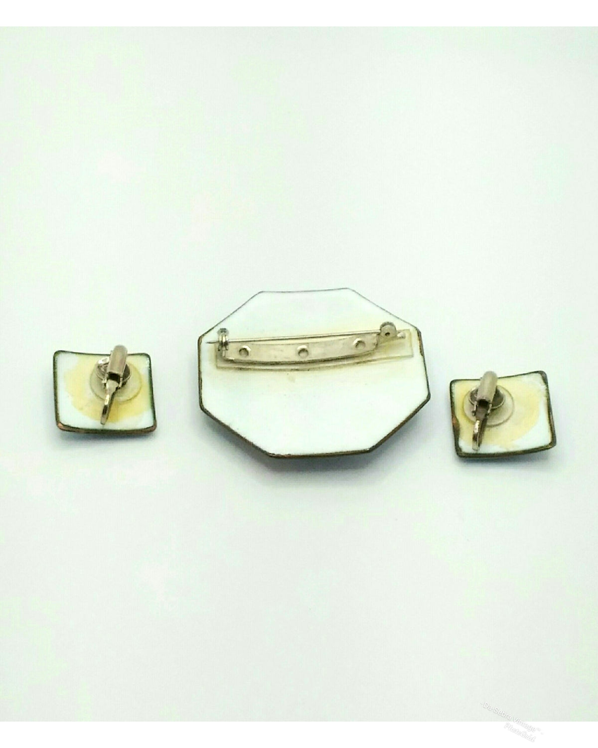 A vintage jewelry set featuring an octagonal enamel pin with a barrette clasp, flanked by two square enamel clip-on earrings with gold-toned metal borders and backs, displayed on a plain white background.