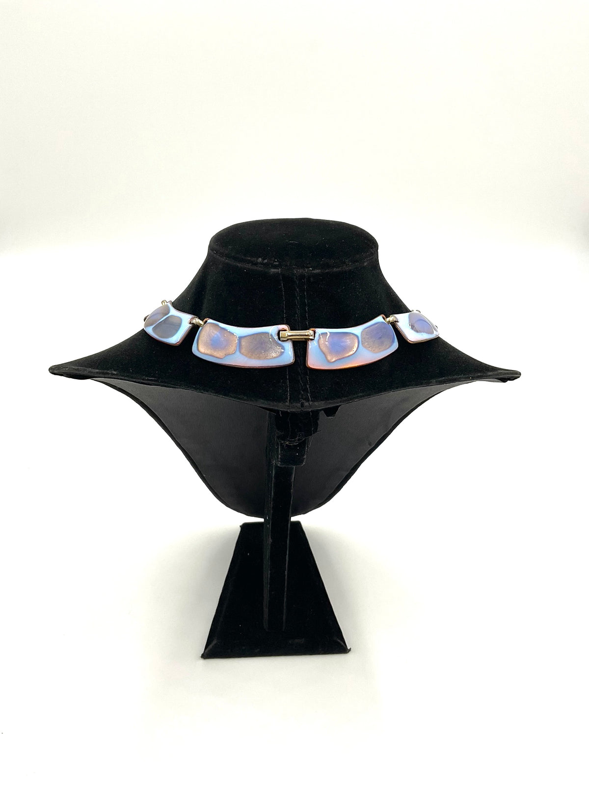 The necklace color palette is exceptional: a striking opalescent blue enamel with beautiful hints of lavender and purple tones, displayed on a black velvet jewelry bust against a white background.