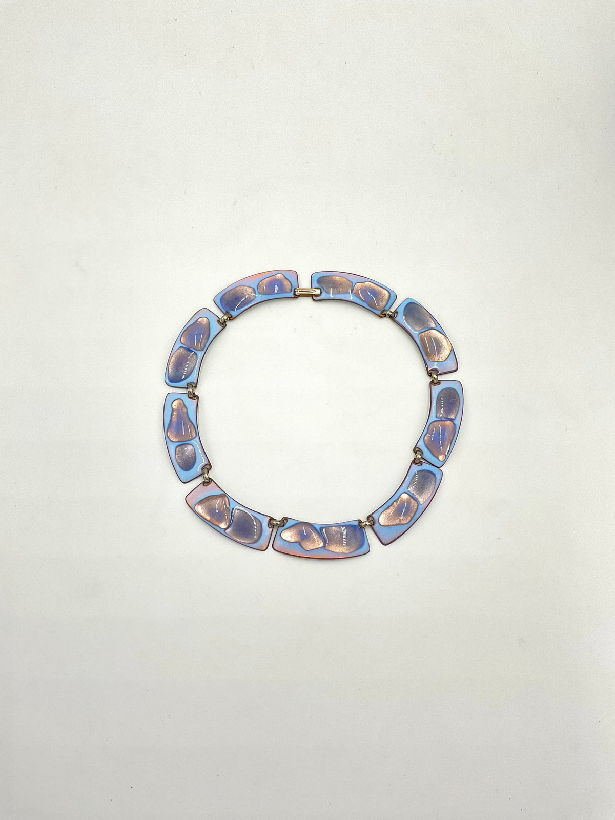 A circular link necklace color palette is exceptional: a striking opalescent blue enamel with beautiful hints of lavender and purple tones metal, displayed on a plain off-white background.