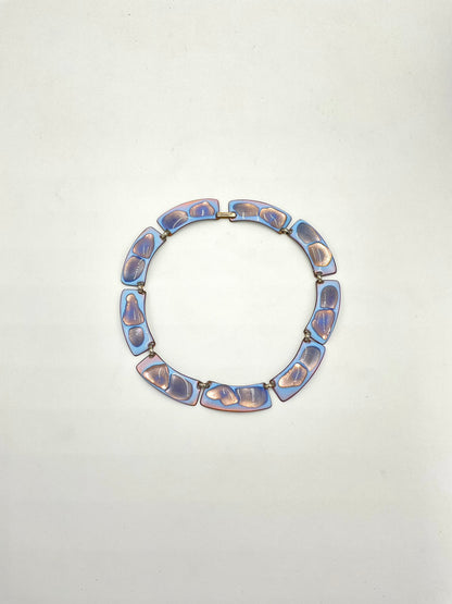 A circular link necklace color palette is exceptional: a striking opalescent blue enamel with beautiful hints of lavender and purple tones metal, displayed on a plain off-white background.