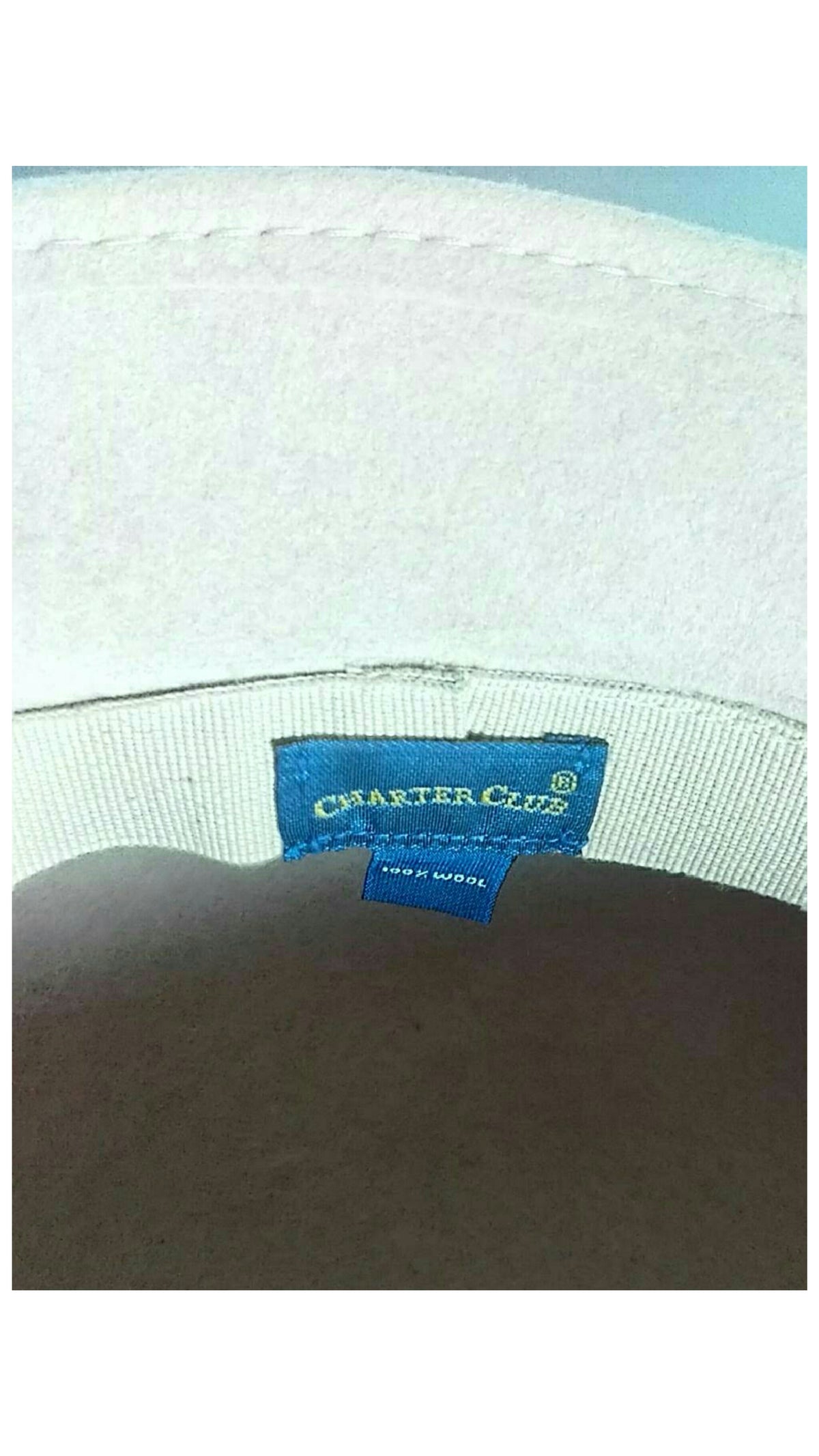 Close-up of the inside of a light-colored fabric cap showing a blue embroidered label that reads 'CHARTER CLUB'  and 100% wool
