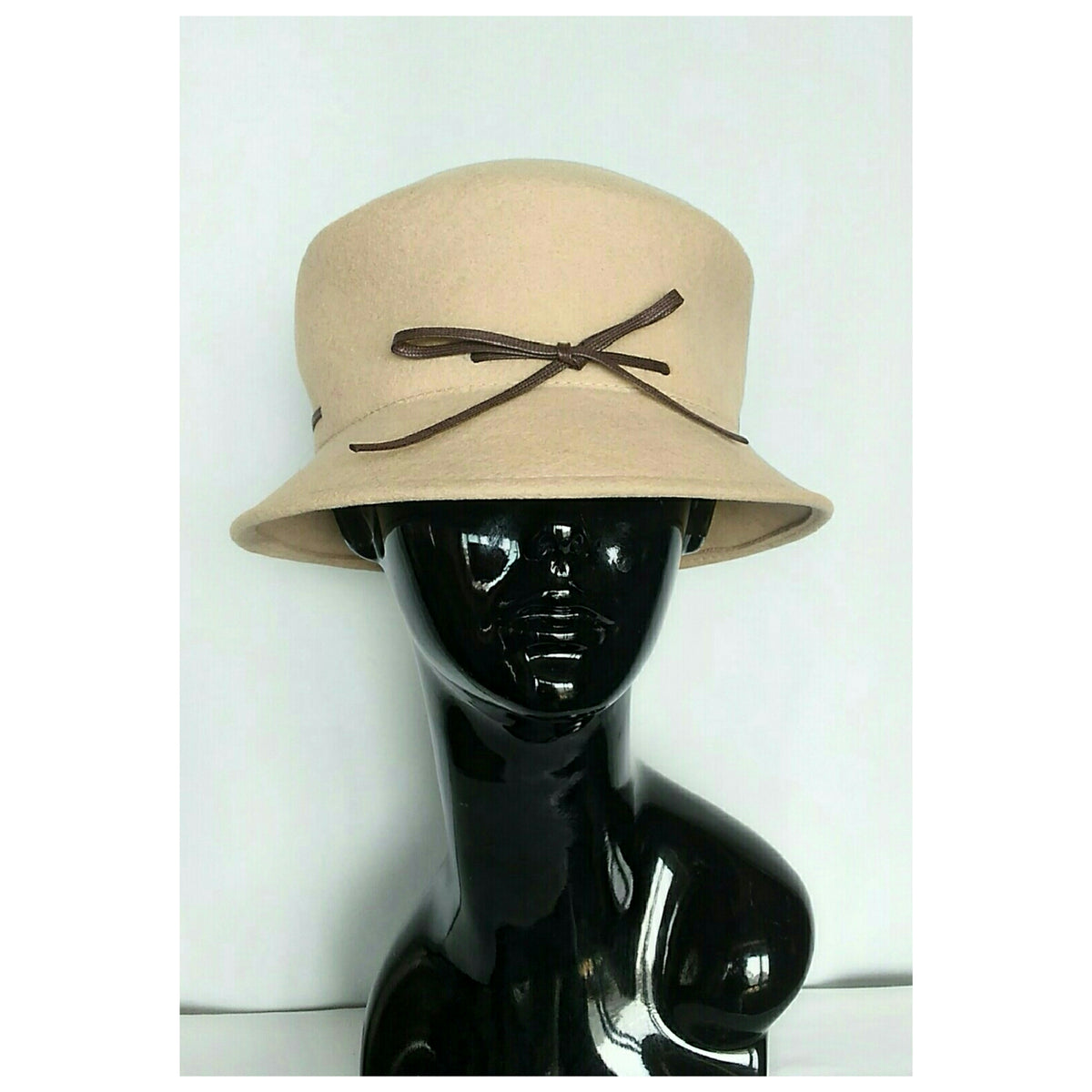 A Camel color felt bucket hat with a dark brown ribbon bow, displayed on a glossy black mannequin head against a plain white background.