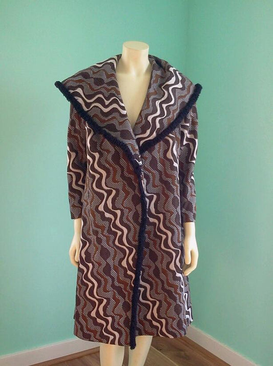 A long-sleeve patterned coat displayed on a mannequin against a mint green wall. The coat features a brown, beige, and black wavy zigzag pattern with a dark fringed collar and front trim.