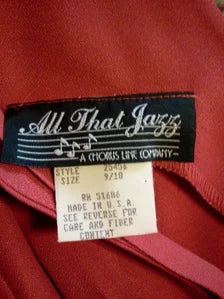 Close-up of a garment's interior neck label reading 'All That Jazz' and 'A Chicos Link Company,' with a red fabric body visible around it.